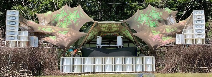 White horn speaker stacks flank a forest festival stage, with subwoofers across the front.