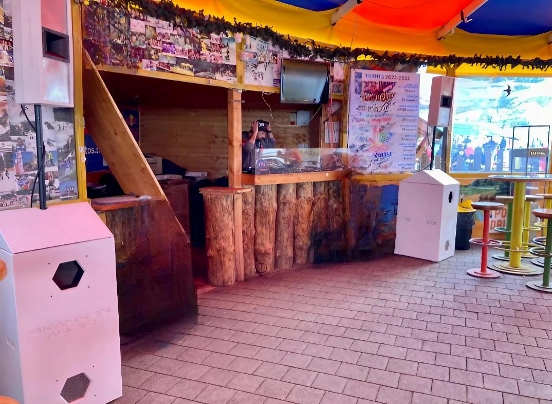 Compact white speaker cabinets and subwoofers installed beside a wooden booth.